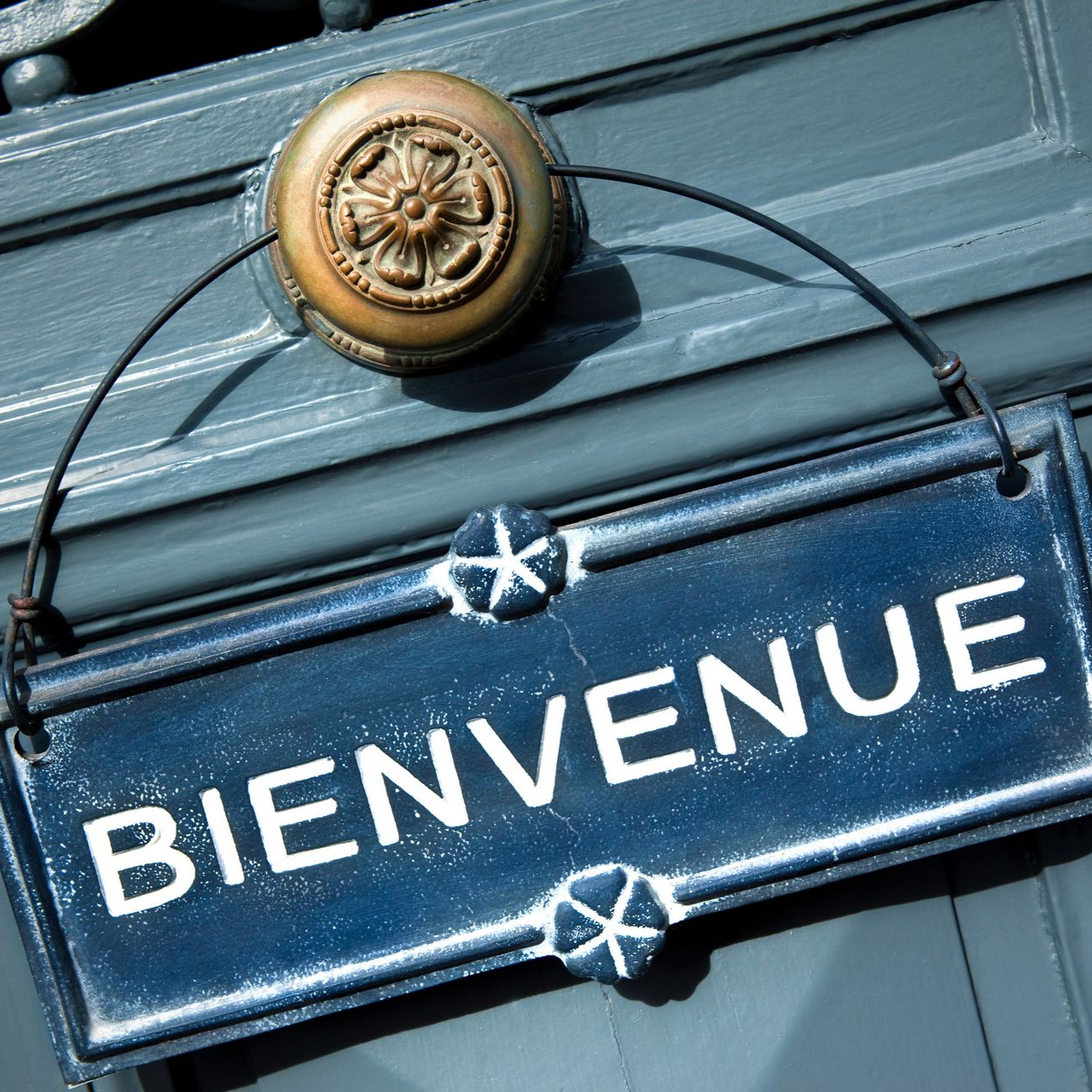 Panneau bleu Bienvenue accroché à une porte bleue avec un heurtoir en laiton.