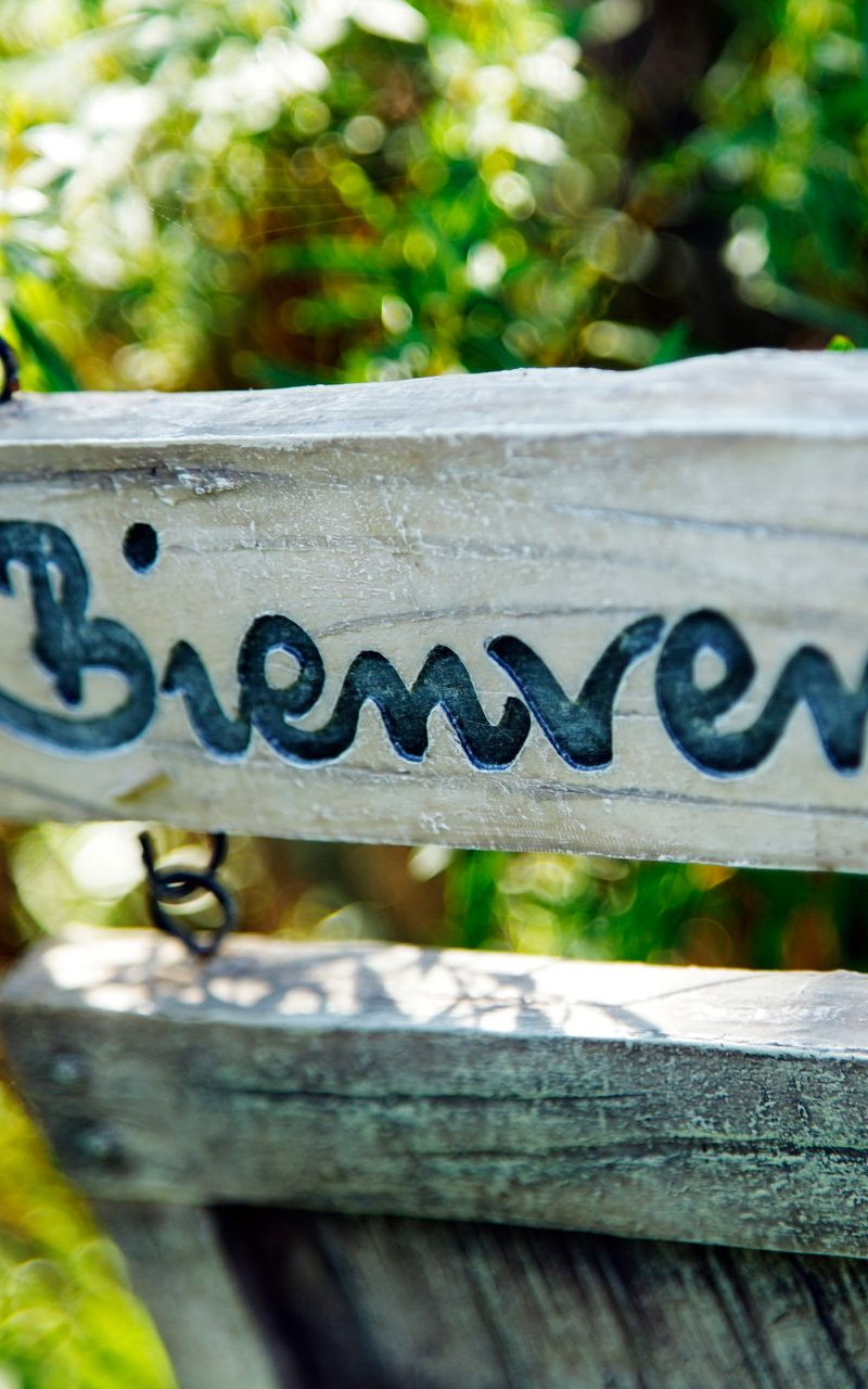 Panneau en bois avec l'inscription Bienvenue gravée en bleu foncé, suspendu dans un jardin.