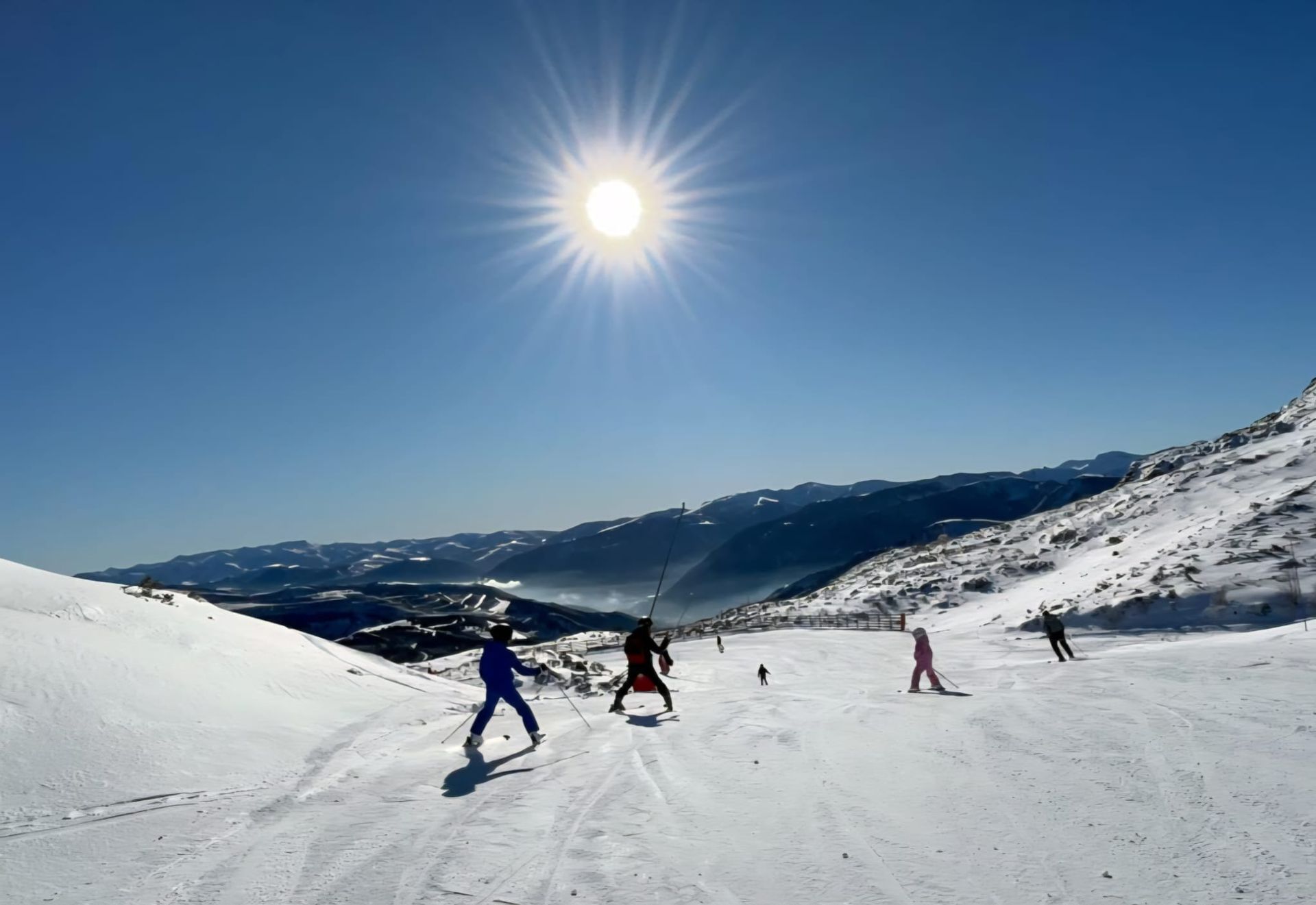 Pistas de esquí nevadas con esquiadores y remontes con las montañas como telón de fondo.