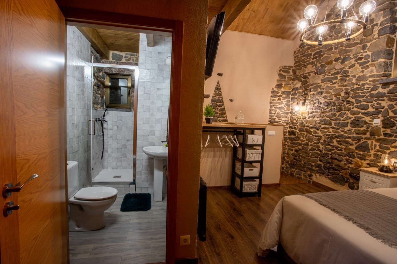 Dormitorio con pared de piedra, baño visible a través de la puerta, suelos de madera.