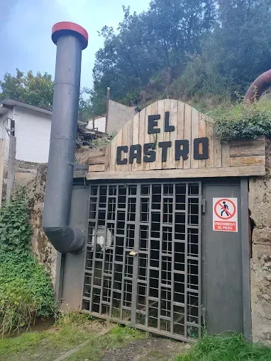 Entrada a mina “El Castro”, portón metálico, letrero, chimenea y cartel de advertencia frente a ladera.