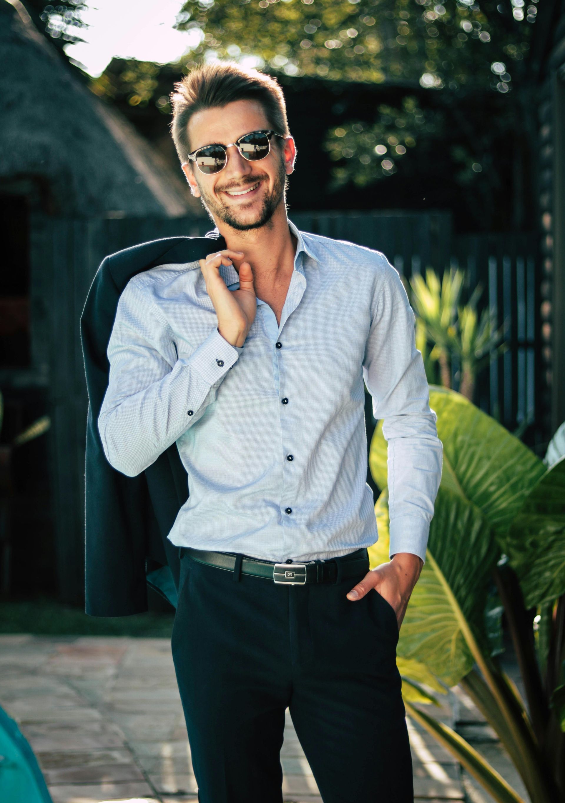 Un uomo che indossa occhiali da sole e una camicia bianca tiene la giacca sopra la spalla.