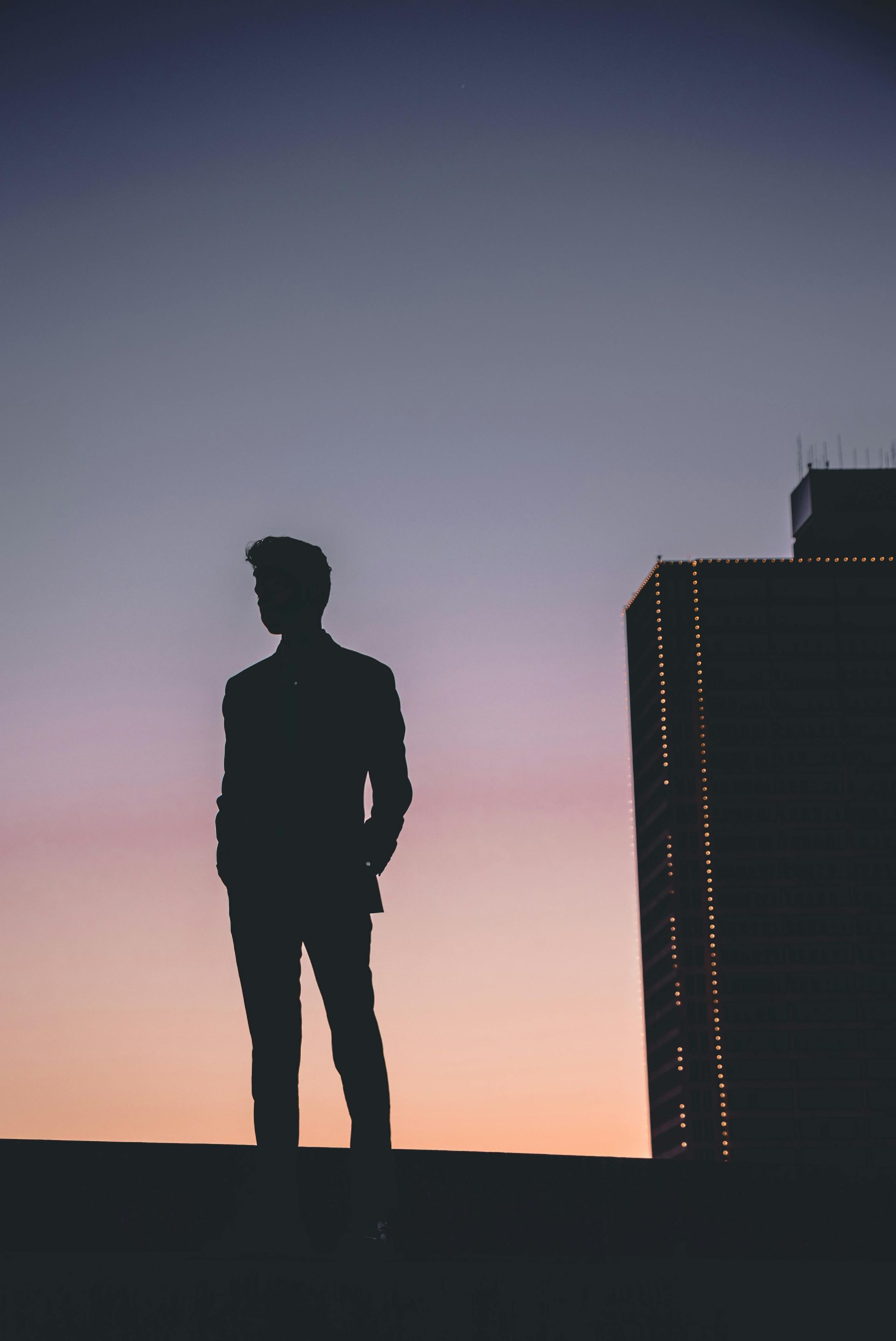La sagoma di un uomo in piedi in cima a un edificio al tramonto.