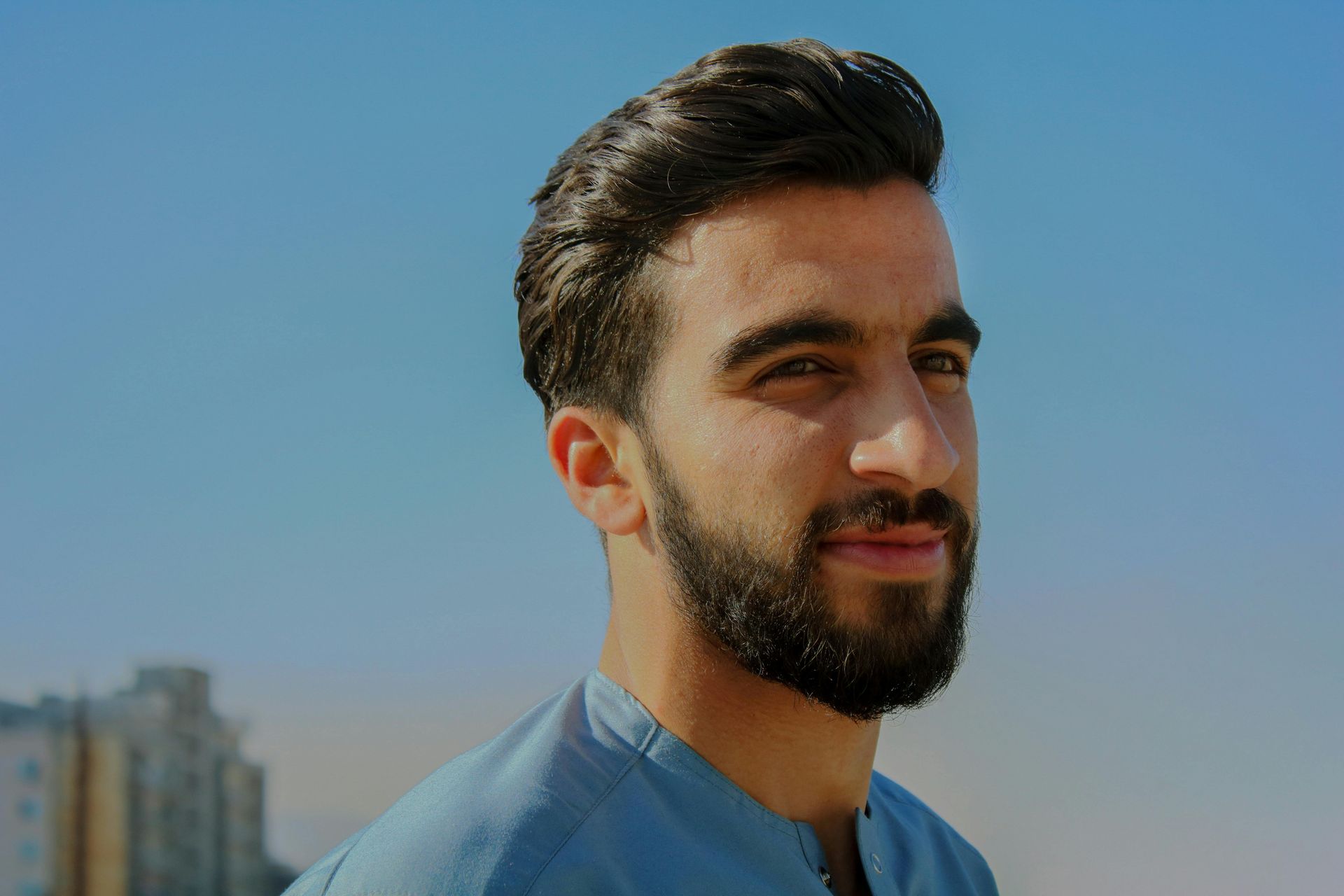 Un uomo con la barba indossa una camicia blu e guarda la telecamera.