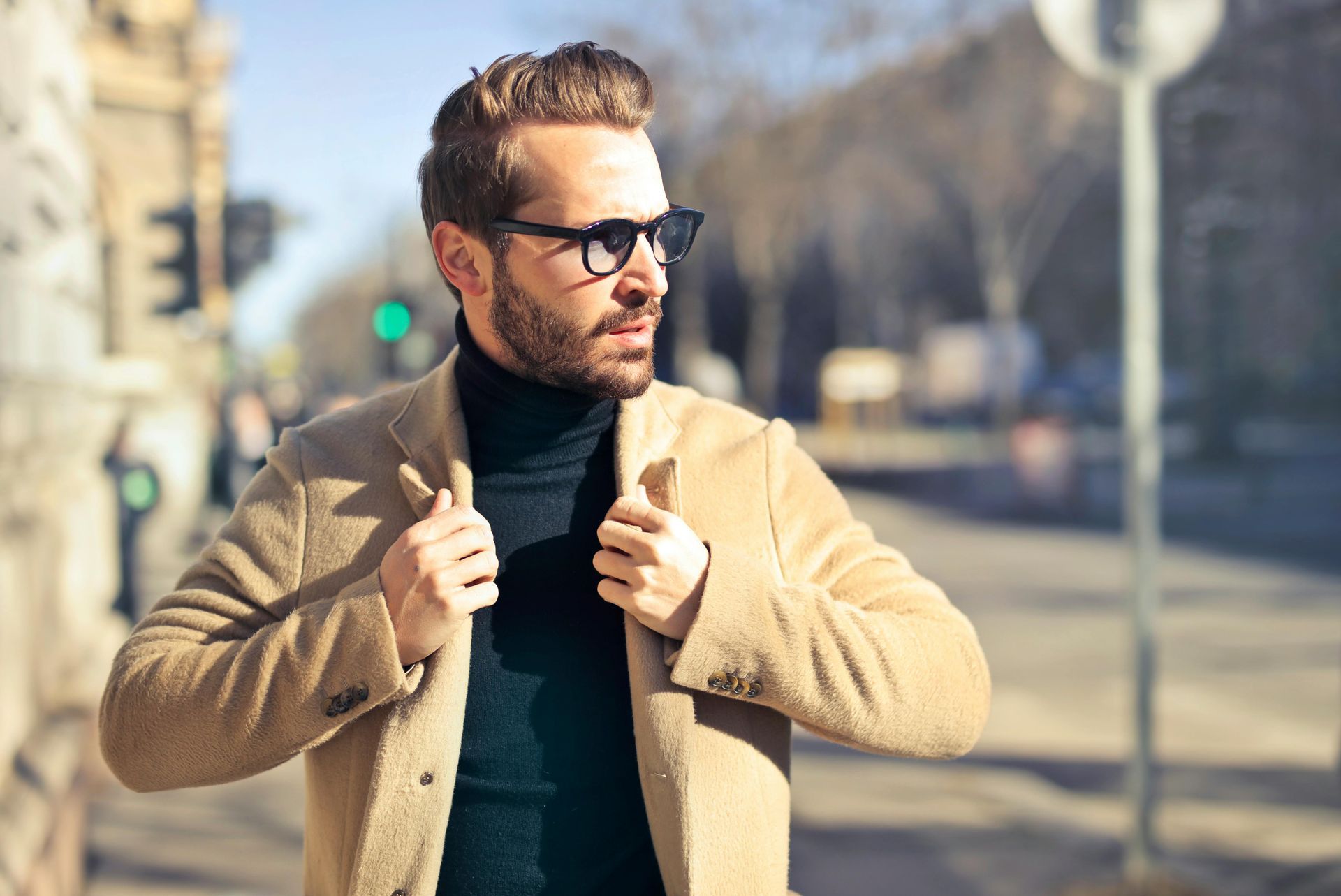Un uomo che indossa un dolcevita e un cappotto è in piedi su una strada cittadina.