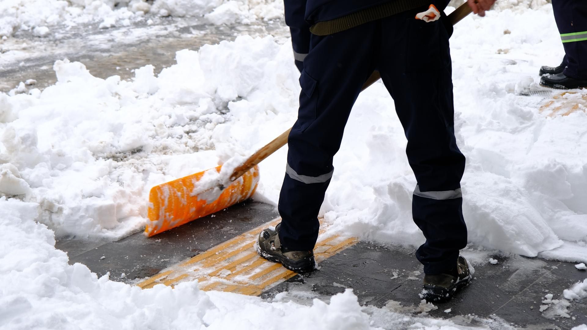 Ein Mann schaufelt Schnee mit einer orangefarbenen Schaufel