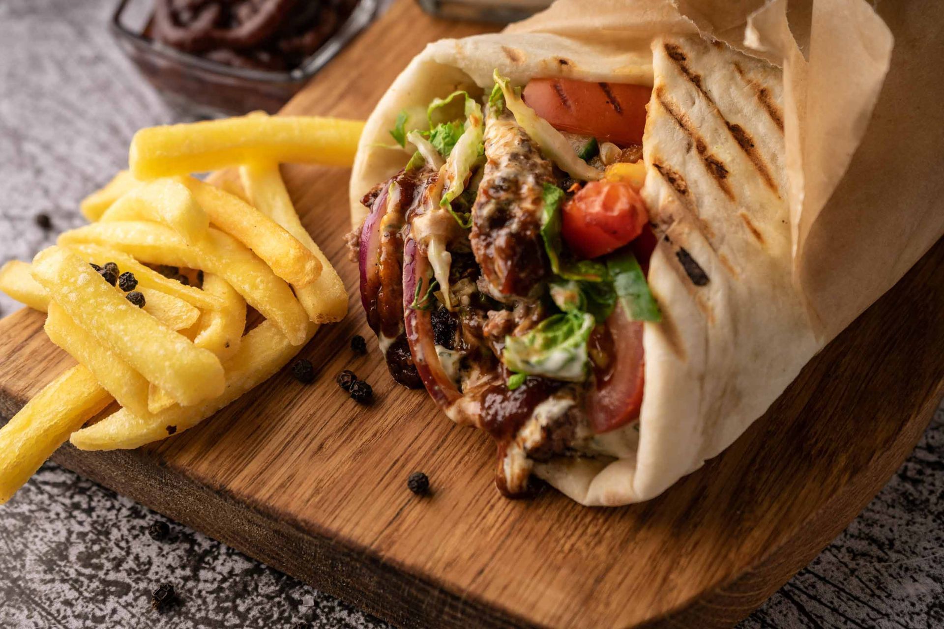 Primer plano de un wrap de shawarma con papas fritas sobre una tabla de madera. El wrap está relleno de carne, verduras y salsa, y se encuentra junto a una porción de papas fritas doradas.