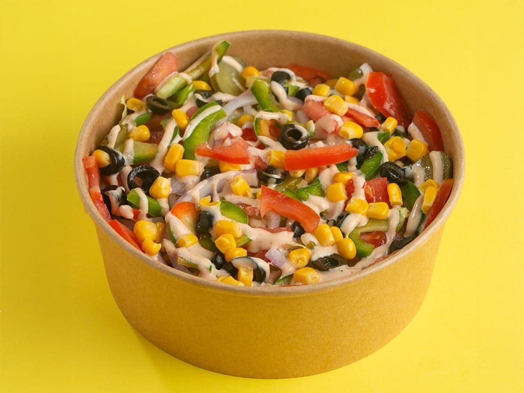 Ensalada con maíz, aceitunas, tomates y aderezo en un recipiente amarillo sobre fondo amarillo.