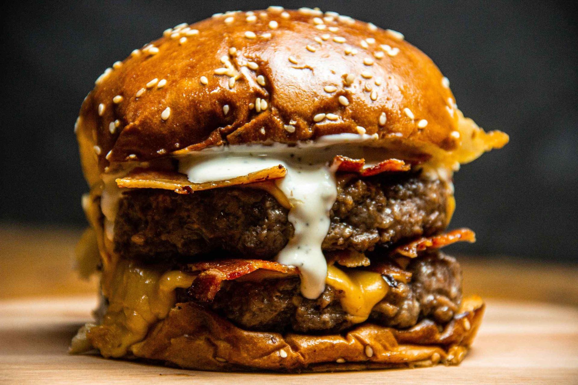 Hamburguesa doble con tocino, queso y salsa en pan con semillas de sésamo. La hamburguesa reposa sobre una superficie de madera.