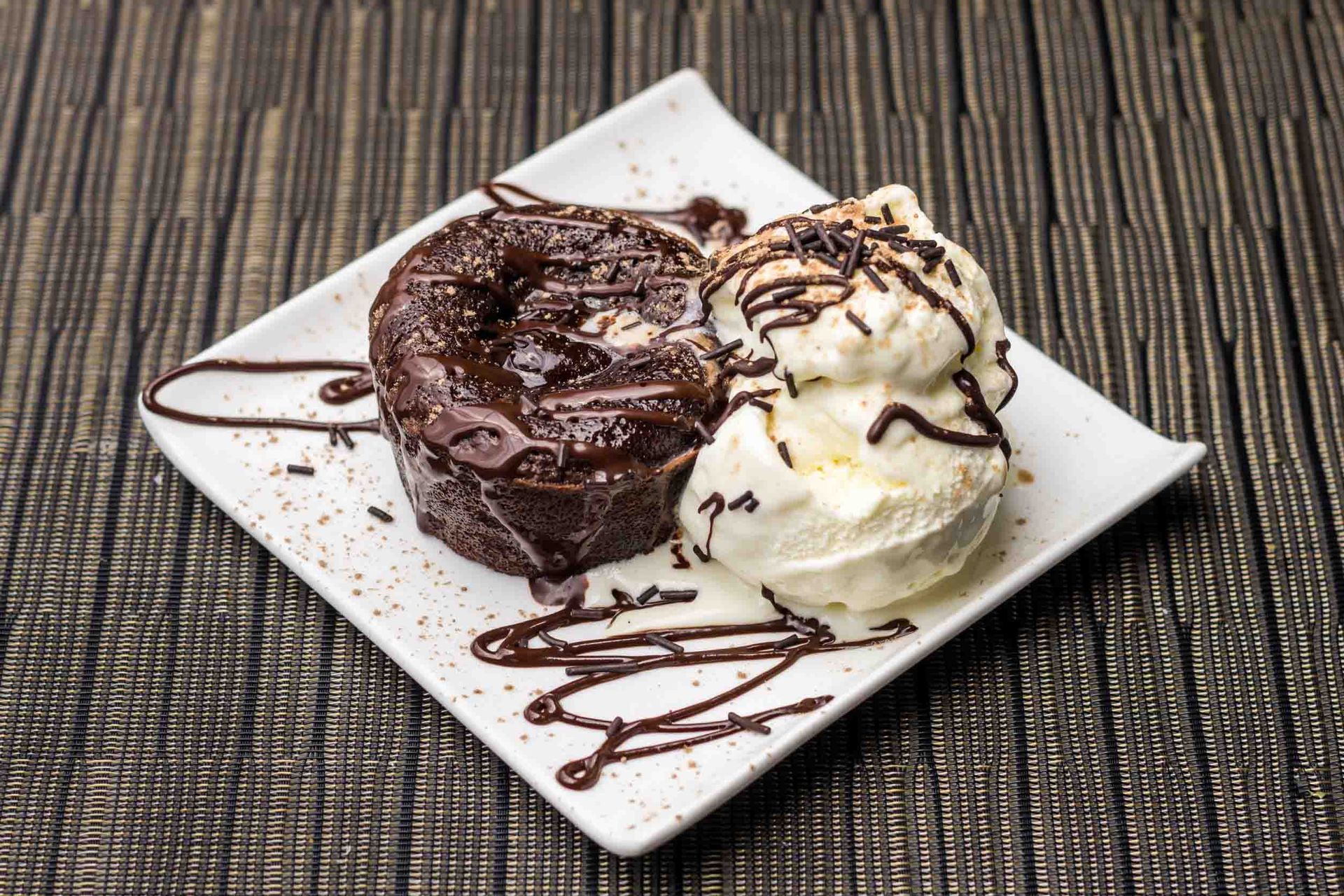Pastel de lava de chocolate con helado de vainilla rociado con jarabe de chocolate en un plato blanco.
