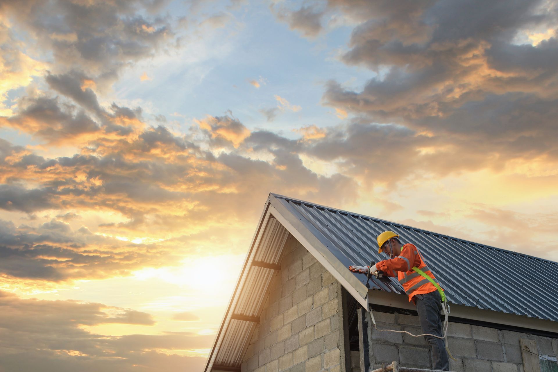 Artisan sur une échelle travaille sur une toiture en bac acier, au coucher du soleil.