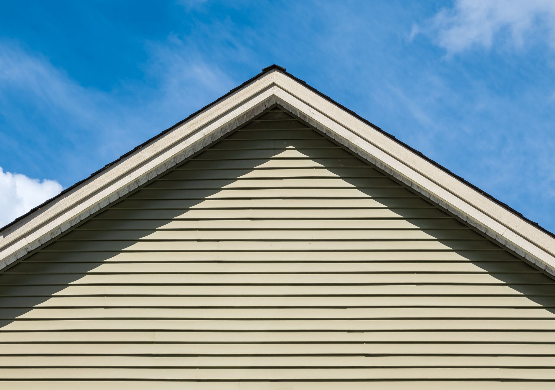 Pignon de maison avec bardage beige sur fond de ciel bleu.