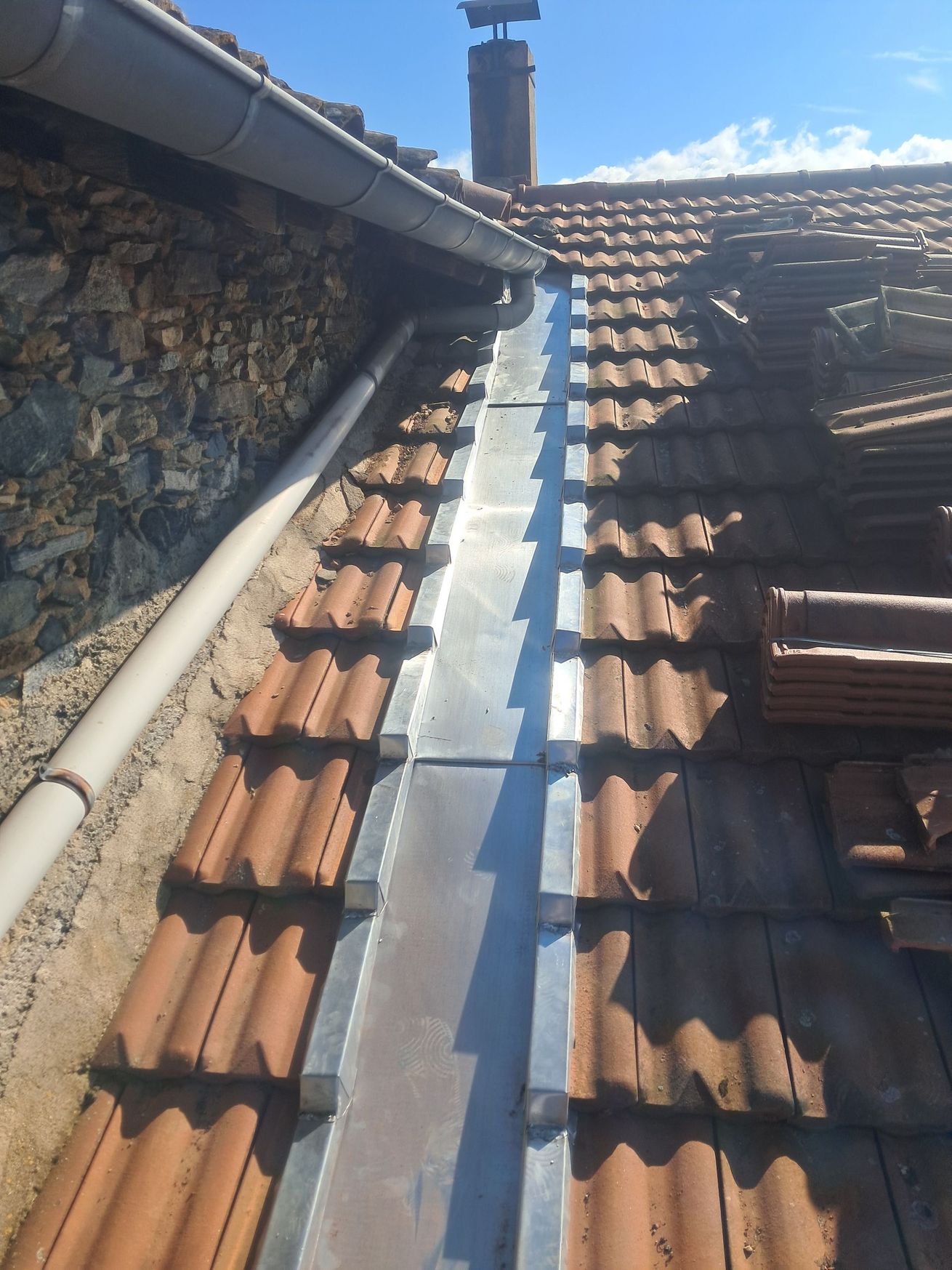Gouttière et descente pluviale fixées à un toit de maison beige avec un bardage en bois en dessous.