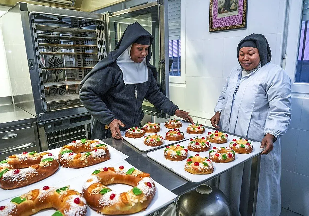 Dos monjas preparando bandejas de pasteles decorados en una cocina comercial.