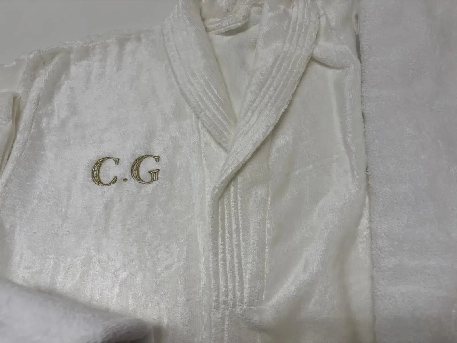 Bata de baño blanca con iniciales “CG” bordadas.