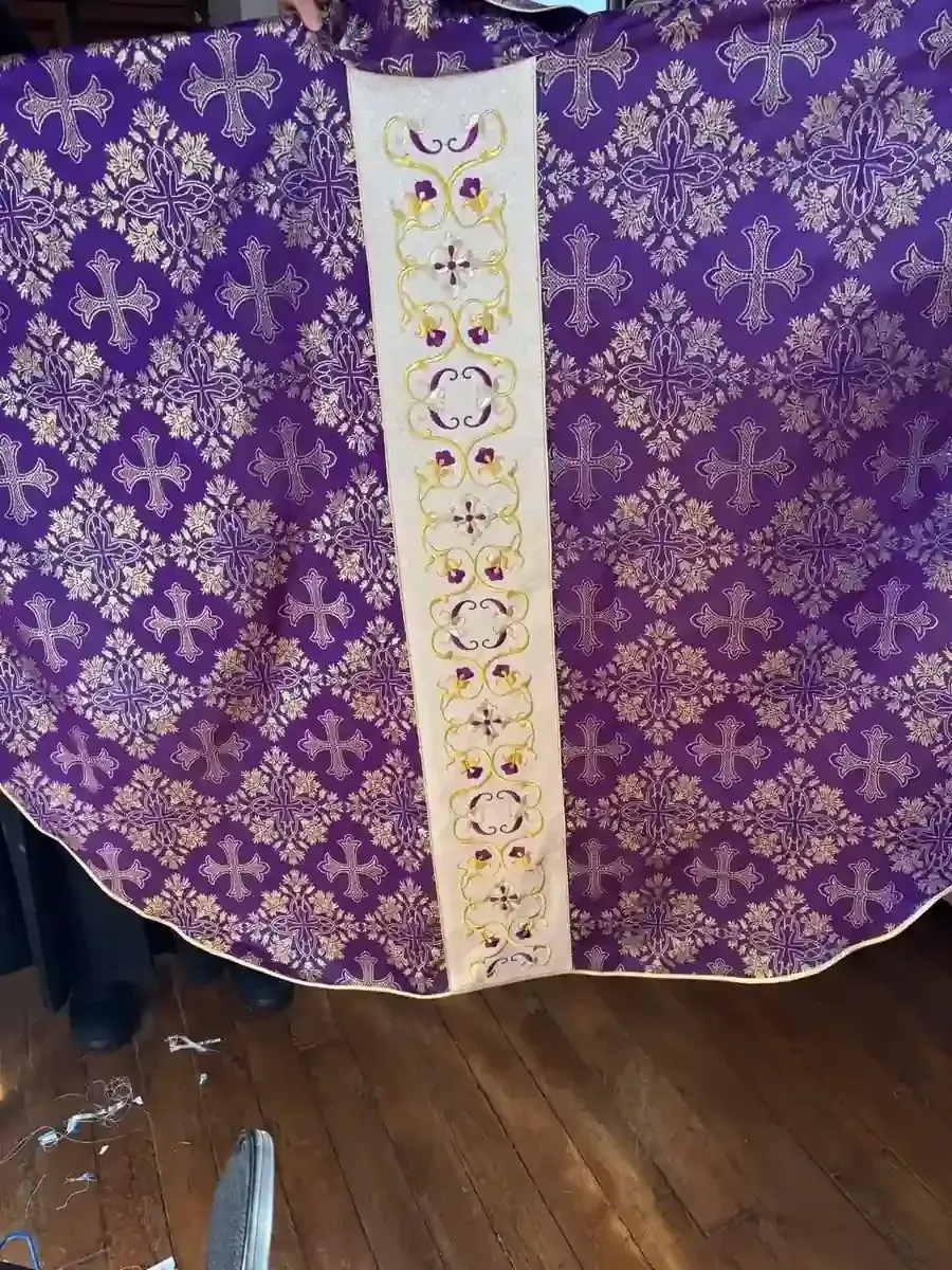 Vestimenta religiosa de color morado y dorado con panel central blanco y dorado, patrón decorativo de cruz.