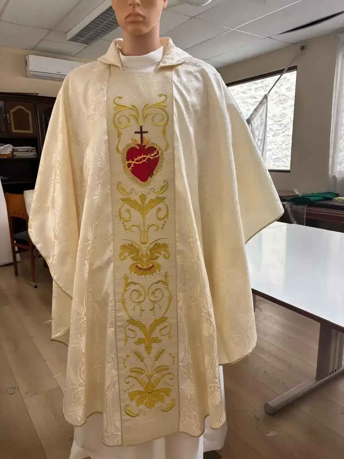 Casulla de marfil con bordado dorado del diseño del Sagrado Corazón, sobre maniquí.