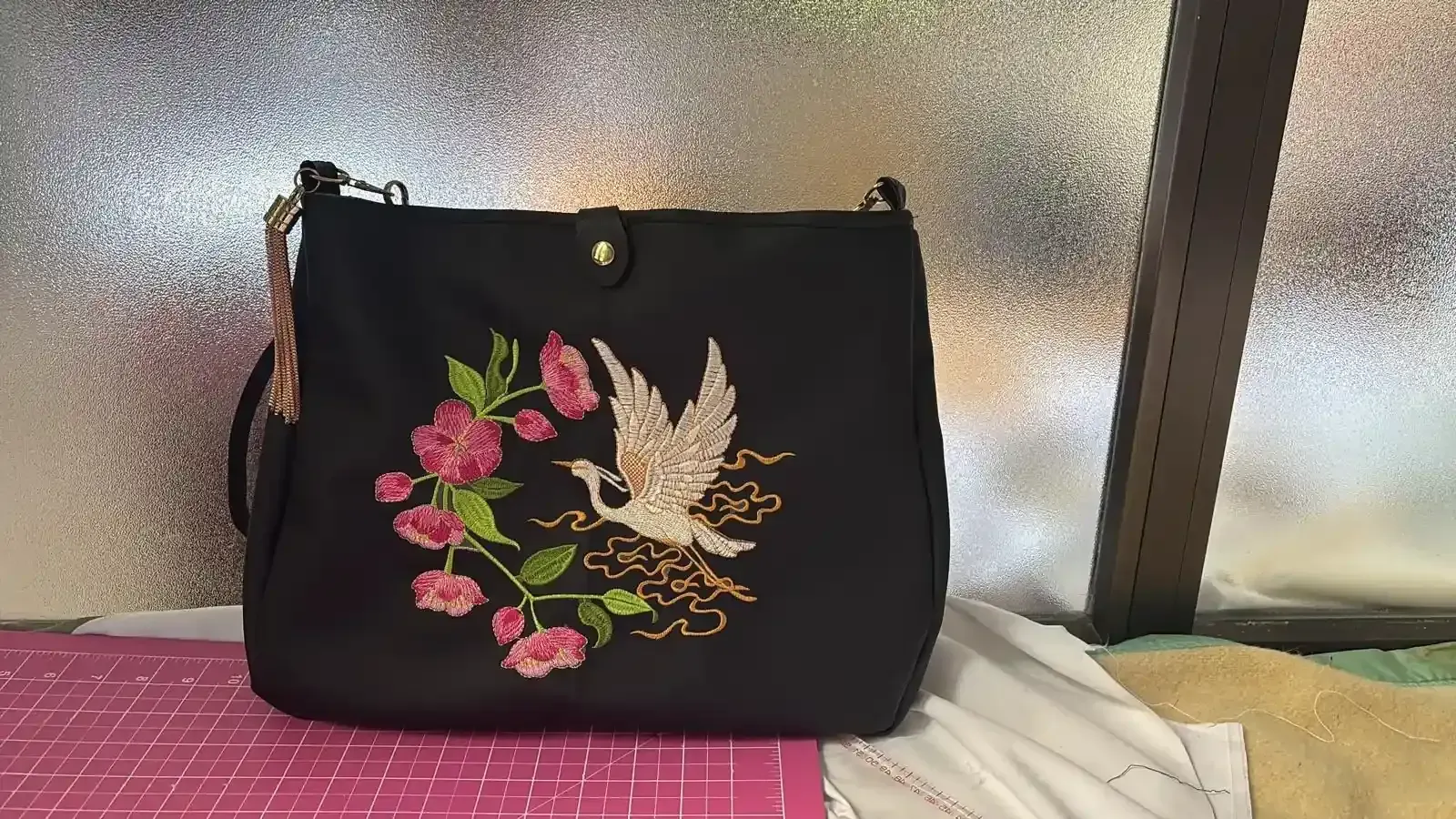 Bolso de hombro negro con grulla bordada y flores; vista frontal.