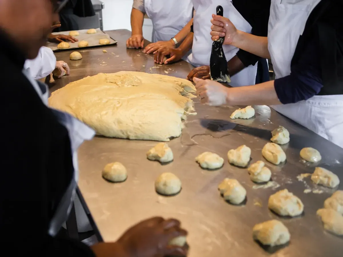 Personas amasando masa sobre una mesa de metal, probablemente preparando productos horneados.