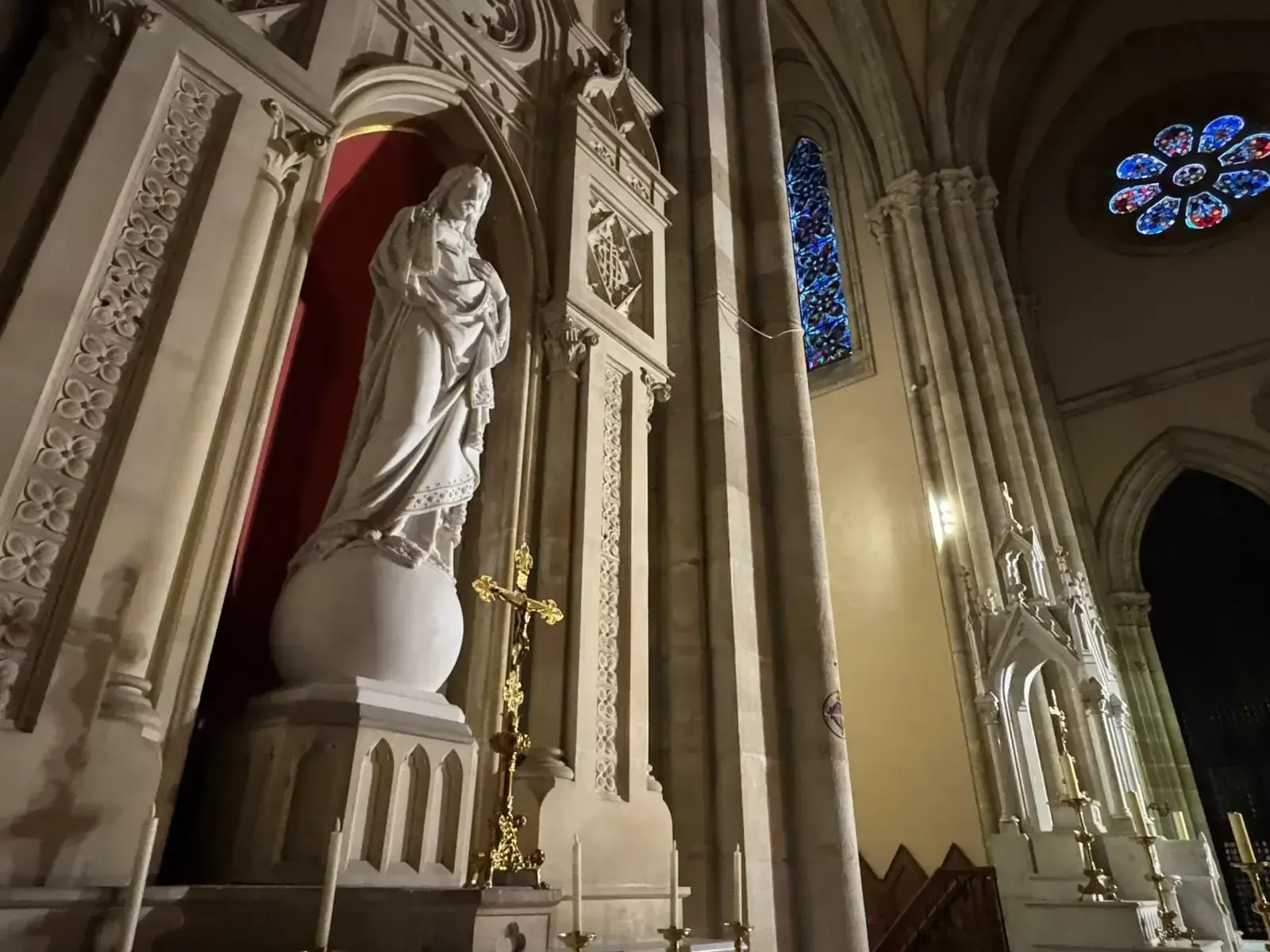 Estatua de una figura religiosa dentro de una iglesia. La estatua es blanca y tiene una cruz dorada cerca.