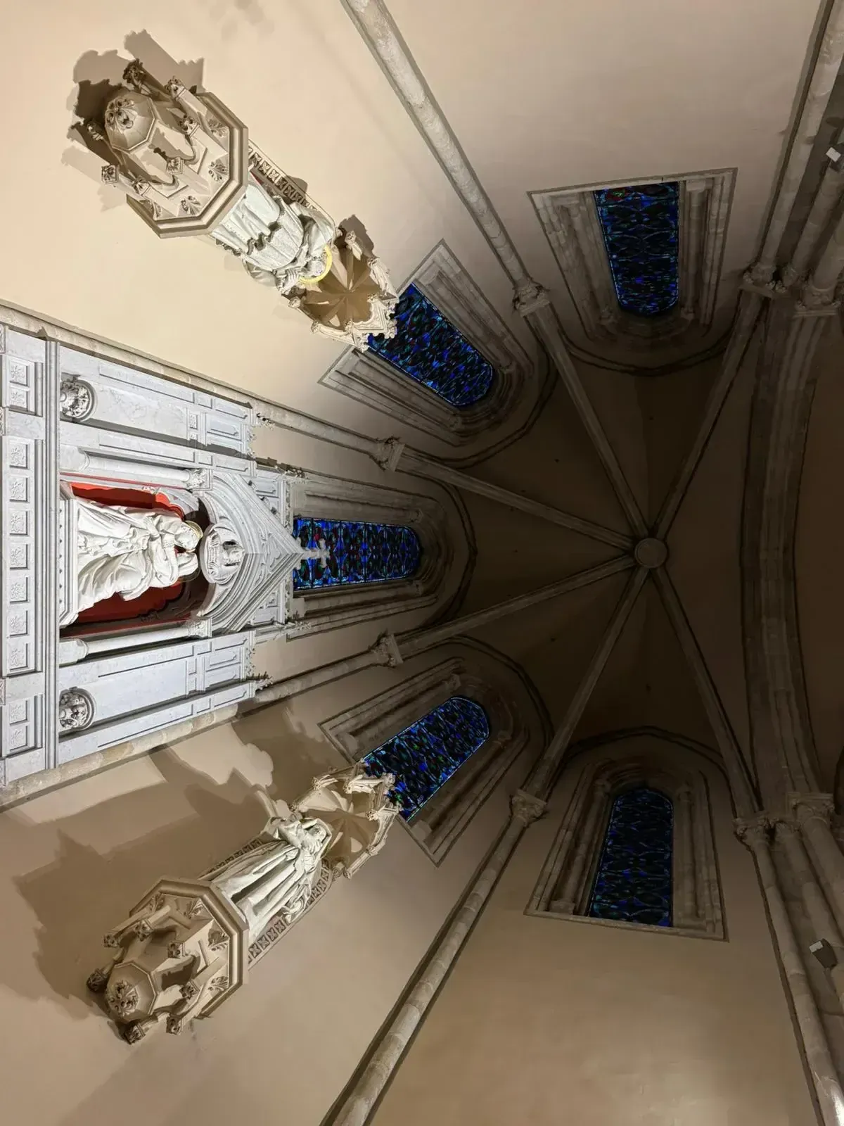 Vista interior de un techo de catedral con tallas ornamentadas, vidrieras y una estatua en una alcoba.