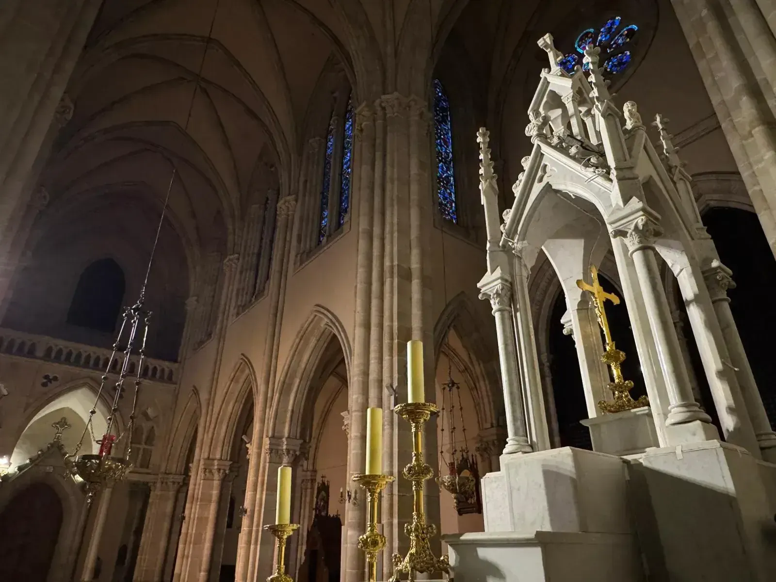 Vista interior de una catedral con arquitectura gótica; arcos, vidrieras y un crucifijo dorado.