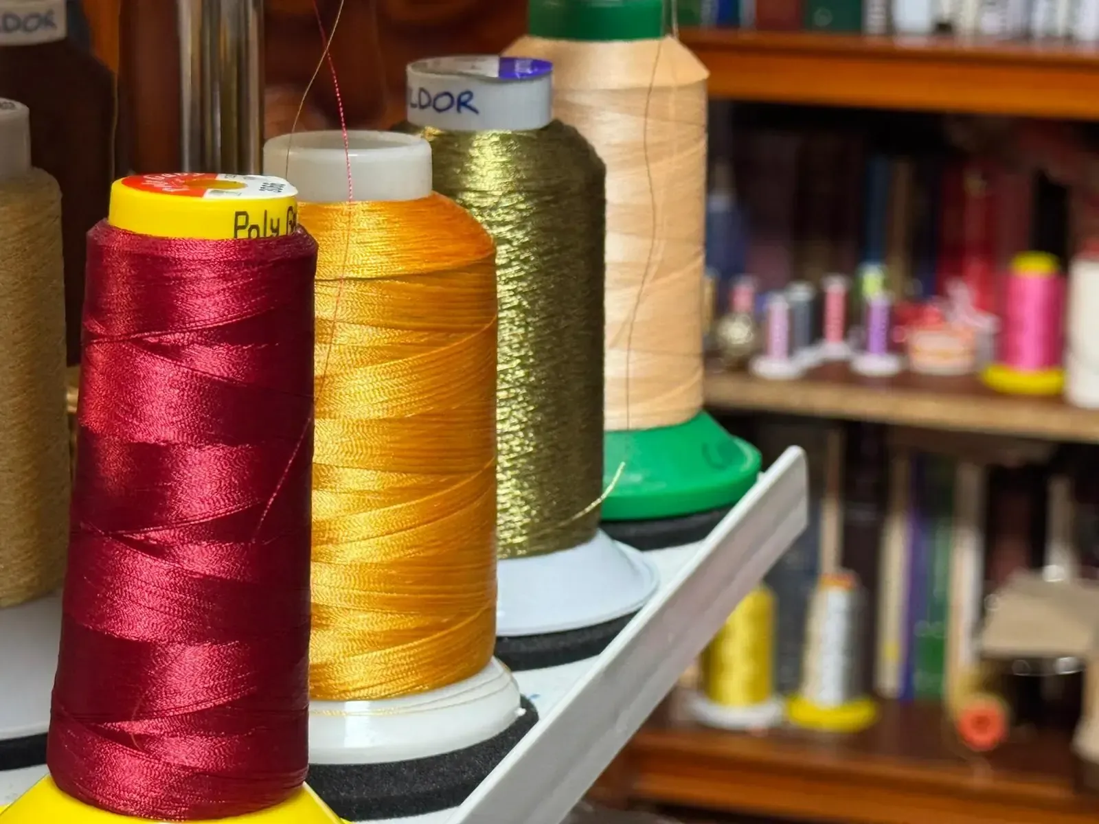 Carretes de hilo de colores en un estante, con un hilo rojo, naranja y dorado en foco.