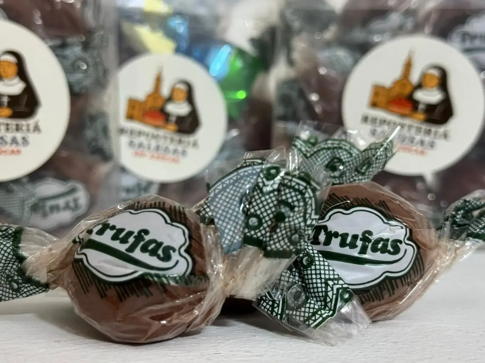 Trufas de chocolate envueltas en papel transparente, etiquetadas con el logo de una monja y torres de iglesia.