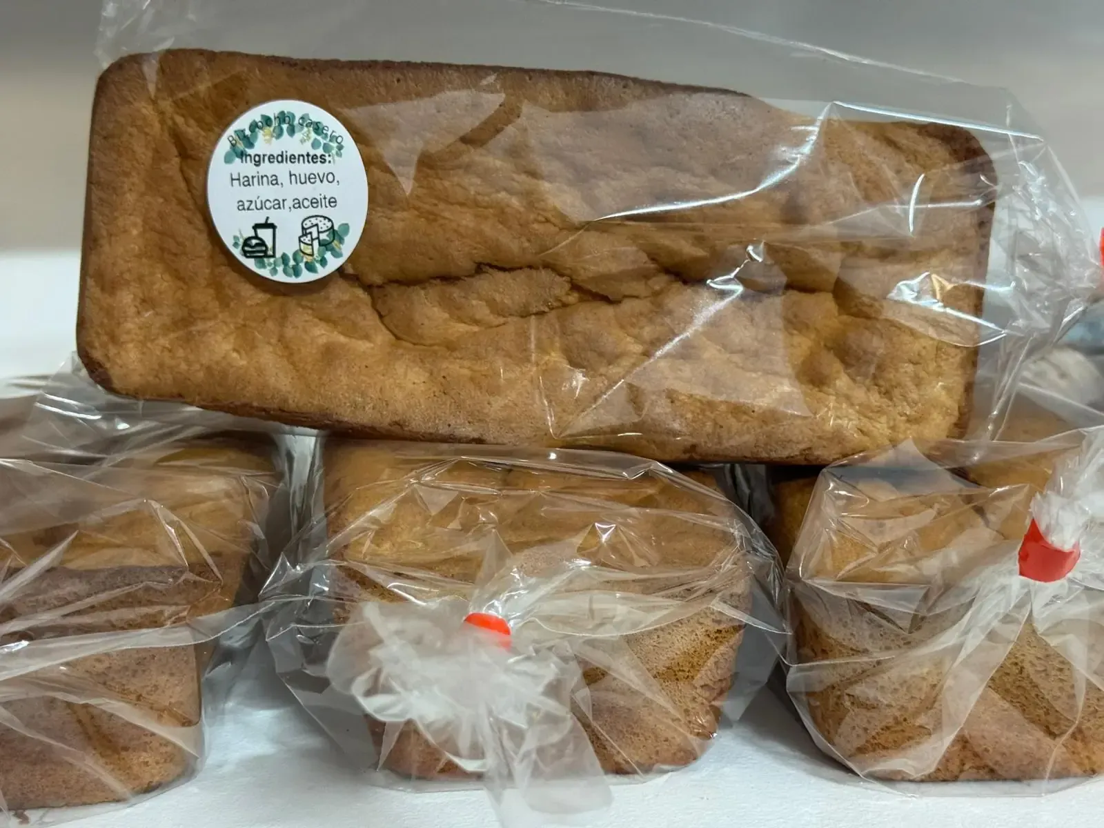 Barras de pan empaquetadas, de color canela, apiladas sobre una superficie. Una barra tiene una etiqueta circular.