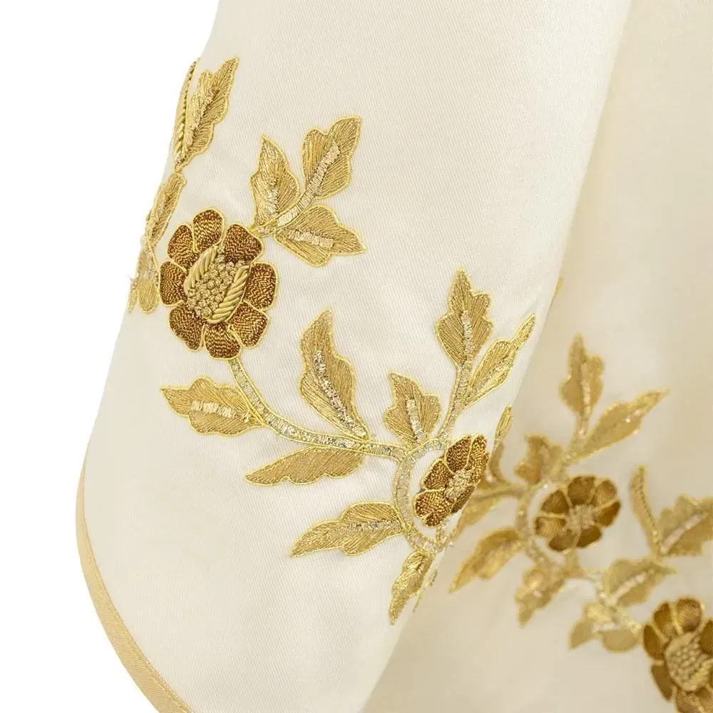Primer plano de una tela blanca con motivos florales y de hojas bordados en oro.