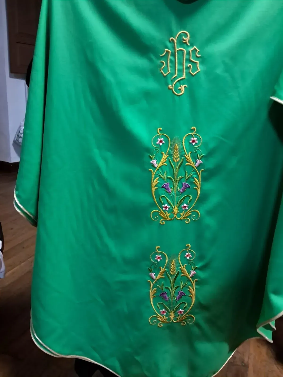 Casulla litúrgica verde con bordados dorados: símbolo IHS y diseños florales.