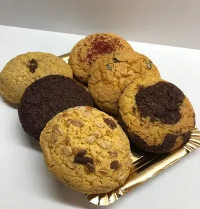 Surtido de galletas de colores en un plato dorado. Diversos sabores y coberturas, incluyendo chocolate, nueces y especias.