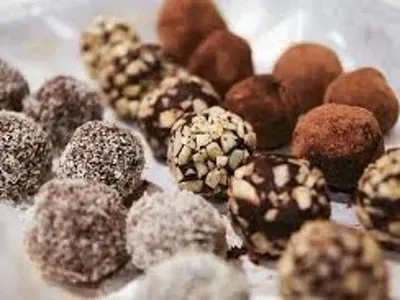 Primer plano de trufas de chocolate surtidas con distintos recubrimientos, dispuestas sobre una superficie blanca.