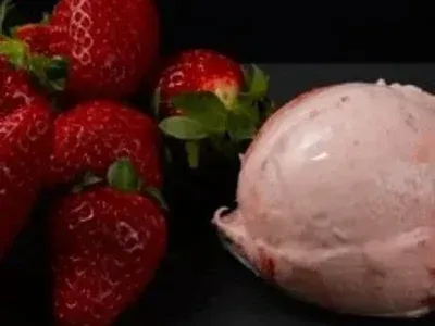 Fresas junto a una bola de helado de fresa rosa sobre una superficie negra.