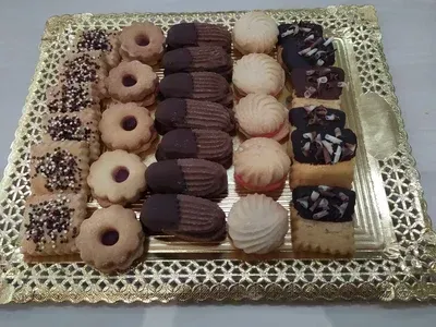 Bandeja de galletas surtidas, incluidas variedades bañadas en chocolate, rellenas de mermelada y espolvoreadas, dispuestas en una bandeja dorada.