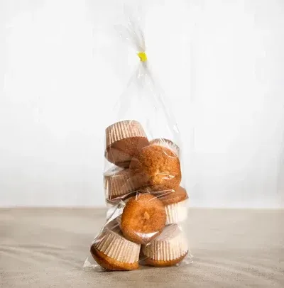 Bolsa de muffins, envuelta en plástico transparente, atada con un lazo amarillo, sobre una superficie de color canela contra un fondo blanco.