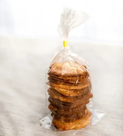 Pila de galletas en una bolsa de plástico transparente, atada con un lazo amarillo, sobre una superficie de color claro.