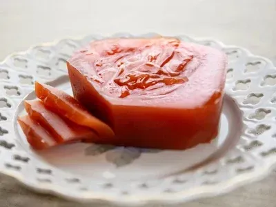 Pasta de membrillo rosa sobre un plato blanco decorativo, con algunas rodajas al lado del bloque principal.