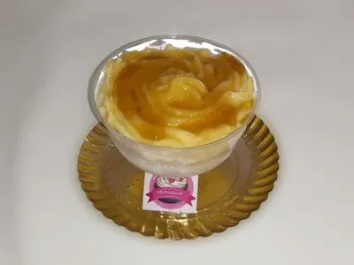 Copa de postre con relleno en espiral de color claro, cubierta con glaseado de caramelo, sobre un plato dorado.