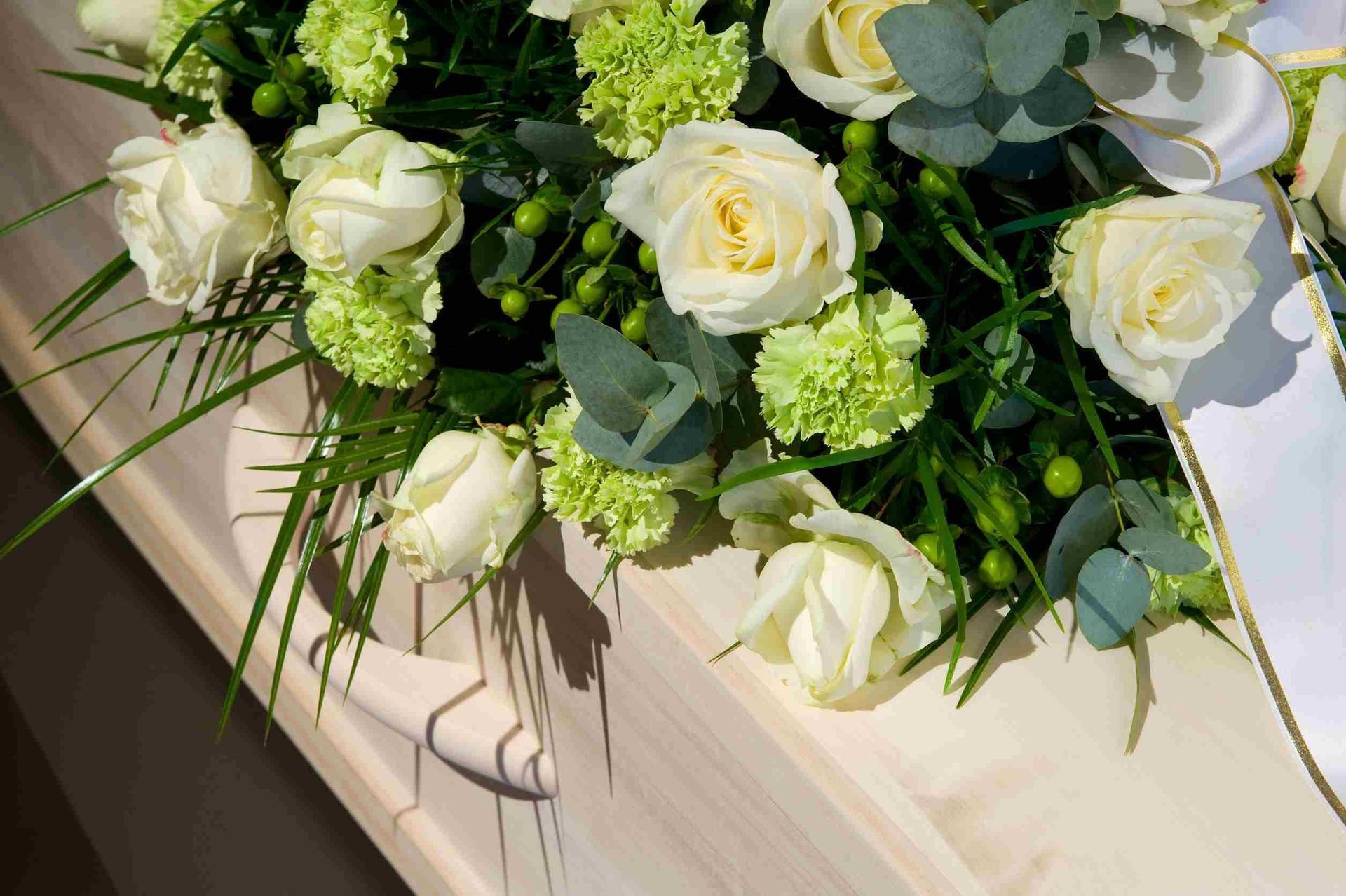 Un ataúd de madera decorado con rosas blancas y claveles verdes.