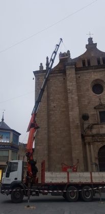 Un camión con grúa trabajando en un gran edificio de piedra con una cruz en la parte superior, bajo un cielo gris.