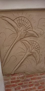 Talla en relieve de flores estilizadas sobre una pared, con una base de ladrillo debajo.