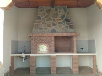 Cocina exterior de ladrillo con chimenea de piedra y fregadero.