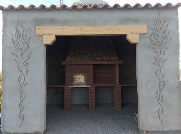 Parrilla de barbacoa de ladrillo dentro de un recinto de hormigón con tallas decorativas de enredaderas y una viga de madera.