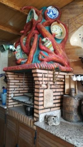 Cocina exterior de ladrillo con una escultura roja en forma de pulpo sobre la parrilla.