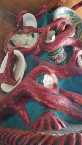 Extremidades esculturales de color rojo con piezas de cerámica reposan sobre una pared turquesa.