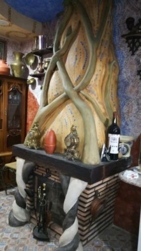 Chimenea con estructura en forma de árbol, base de ladrillo, estantes con ollas y una botella de vino.
