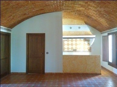 Habitación con techo de ladrillo abovedado, paredes blancas, puertas de madera y suelo de baldosas.