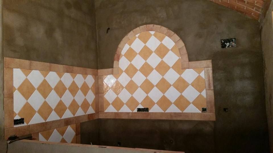 Pared de cocina en construcción, azulejos con estampado de diamantes en tonos beige y blancos, elemento arqueado, borde marrón.