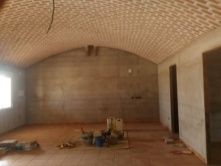 Interior de una habitación en construcción con techo abovedado de ladrillo y paredes y piso sin terminar.